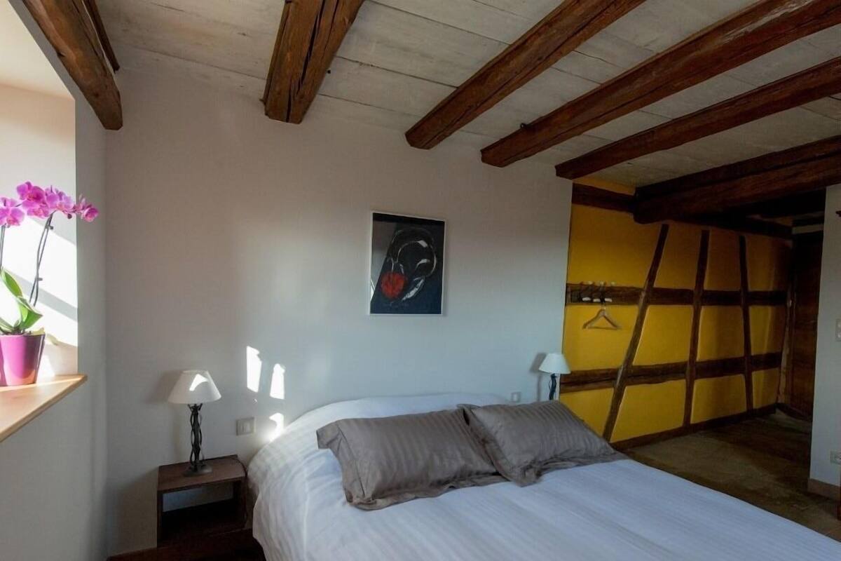 A bedroom with a bed, a nightstand, a lamp, a potted plant, and a painting on the wall.