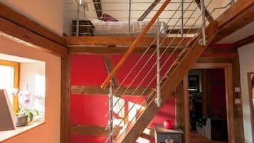 Een kamer met een houten trap, een bed op de bovenverdieping, en een klein tafeltje met een rood voorwerp erop.