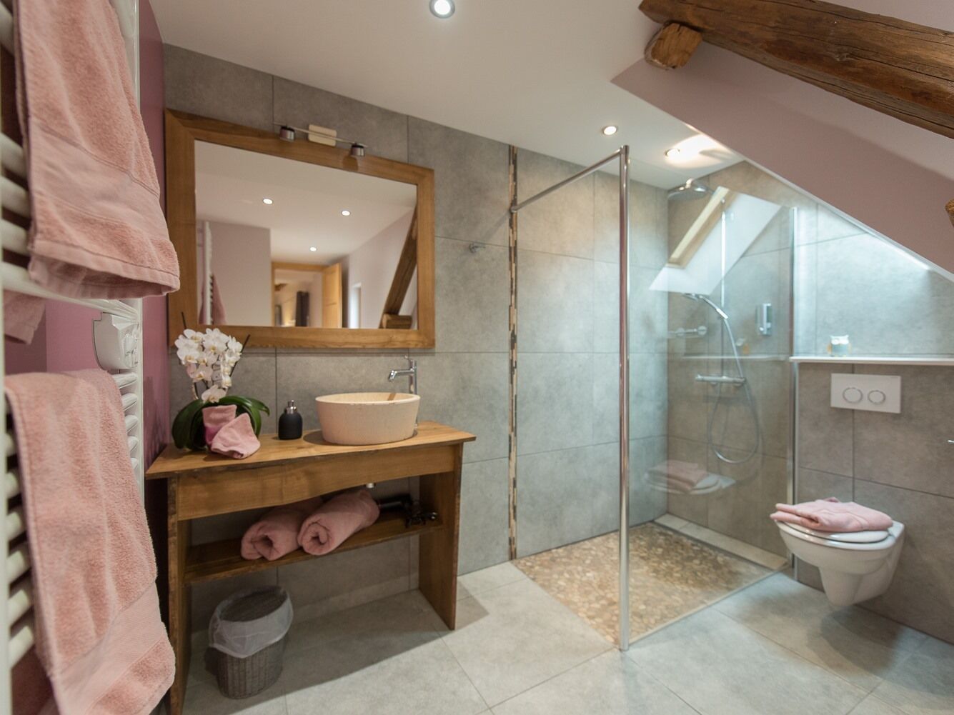 Ein modernes Badezimmer mit einem Holzkosmetikschrank, einem großen Spiegel, einer Duschkabine aus Glas und einer Toilette.