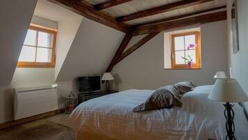 Ein Schlafzimmer mit schrägem Dach, einem Bett, einem Fernseher, einem Fenster mit Pflanze und einer Heizung.