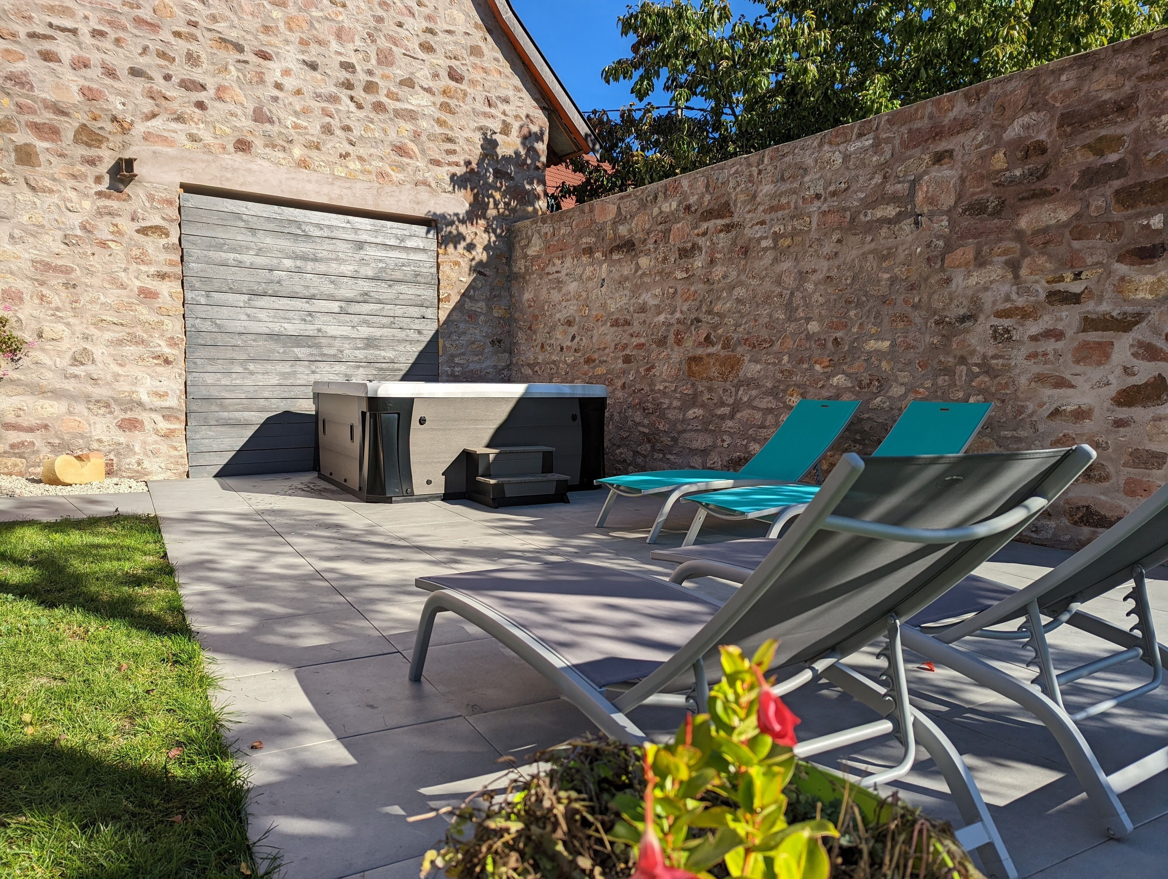 An outdoor patio with a stone wall, a hot tub, and two lounge chairs.