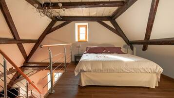 Ein Schlafzimmer mit Holzboden, einem Bett mit weißer und pinkfarbener Bettwäsche, einem Nachttisch und einem Fenster mit Tageslicht.