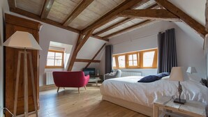 A spacious loft bedroom with a large bed, wooden beams, a red chair, and a television.