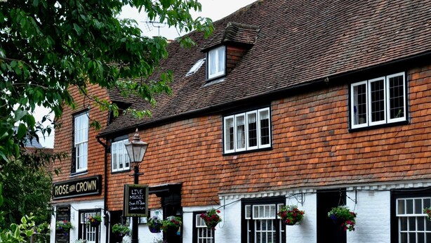 A traditional brick building with a sign for 'Rose and Crown' pub, outdoor seating, and hanging flower baskets. - The Rose & Crown (Etchingham)