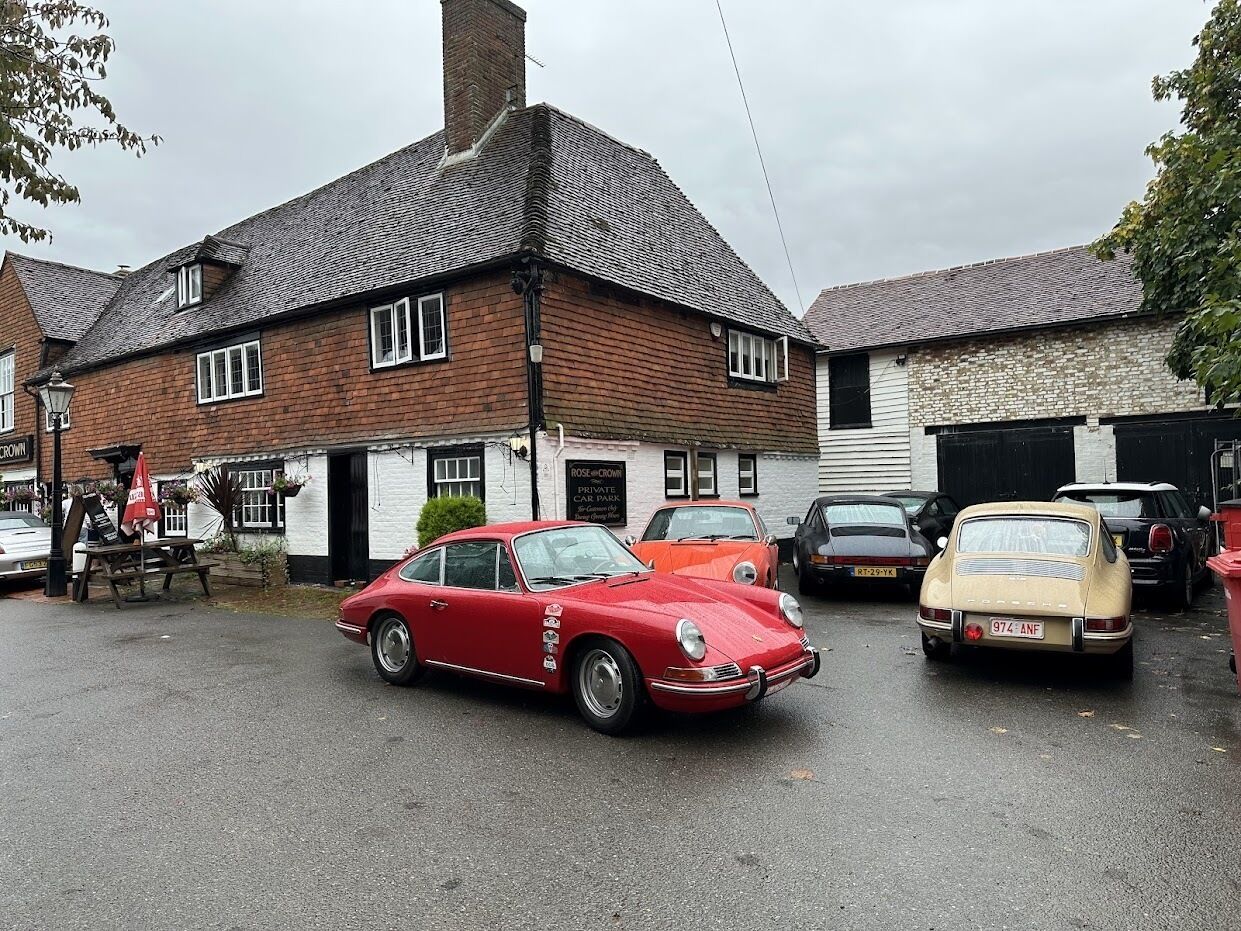 Un coche rojo antiguo estacionado frente a un edificio con un letrero que dice "Rose Crown Private Car Park".