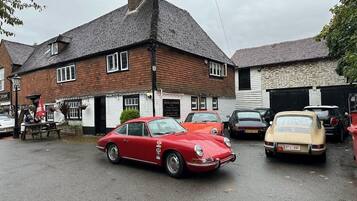 Un coche rojo antiguo estacionado frente a un edificio con un letrero que dice "Rose Crown Private Car Park".