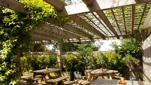 A wooden pergola with a lattice roof, surrounded by lush greenery and multiple wooden picnic tables. - The Rose & Crown (Etchingham)