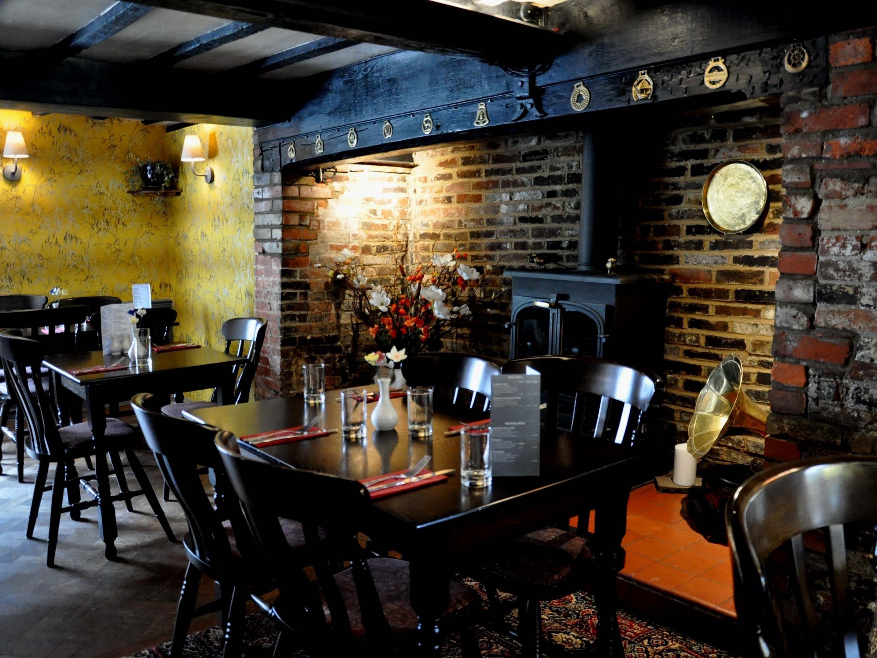 A restaurant with brick walls, wooden beams, and a brick fireplace. Tables and chairs are set up for dining.