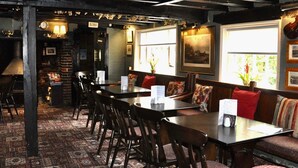 A restaurant with a long wooden table and chairs, a patterned carpet, and a bench with cushions. - The Rose & Crown (Etchingham)