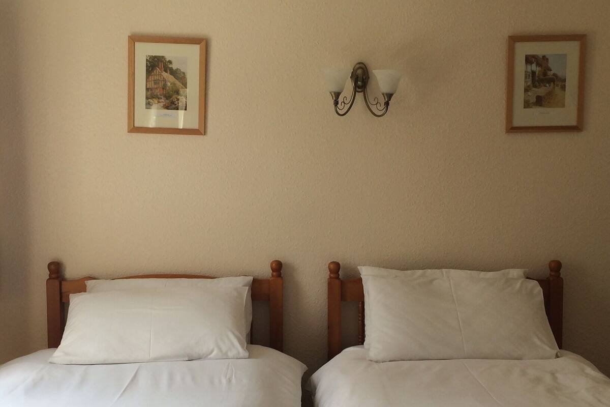 Dos camas individuales con cabeceras de madera, ropa de cama blanca y dos cuadros en la pared.