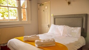A neatly made bed with white and yellow bedding, a grey headboard, and two white pillows. - The Rose & Crown (Etchingham)