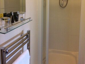 A bathroom with a glass shelf holding toiletries, a towel rack, and a shower area with a glass door. - The Rose & Crown (Etchingham)