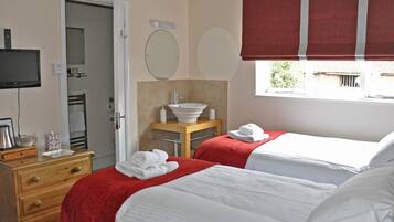 A hotel room with two beds, a wooden dresser, a television, a bathroom with a sink and mirror, and a window with a view.