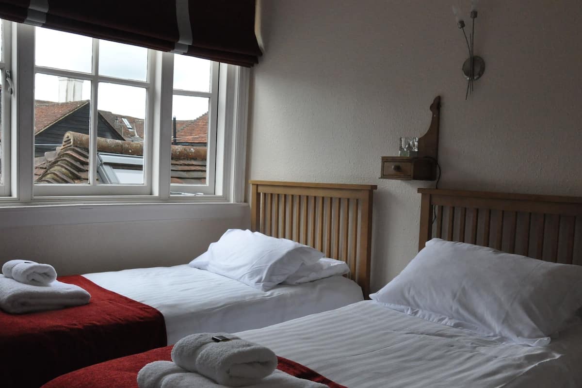 Una habitación de hotel con dos camas, un ventanal con vistas a edificios y un cabecero de madera.