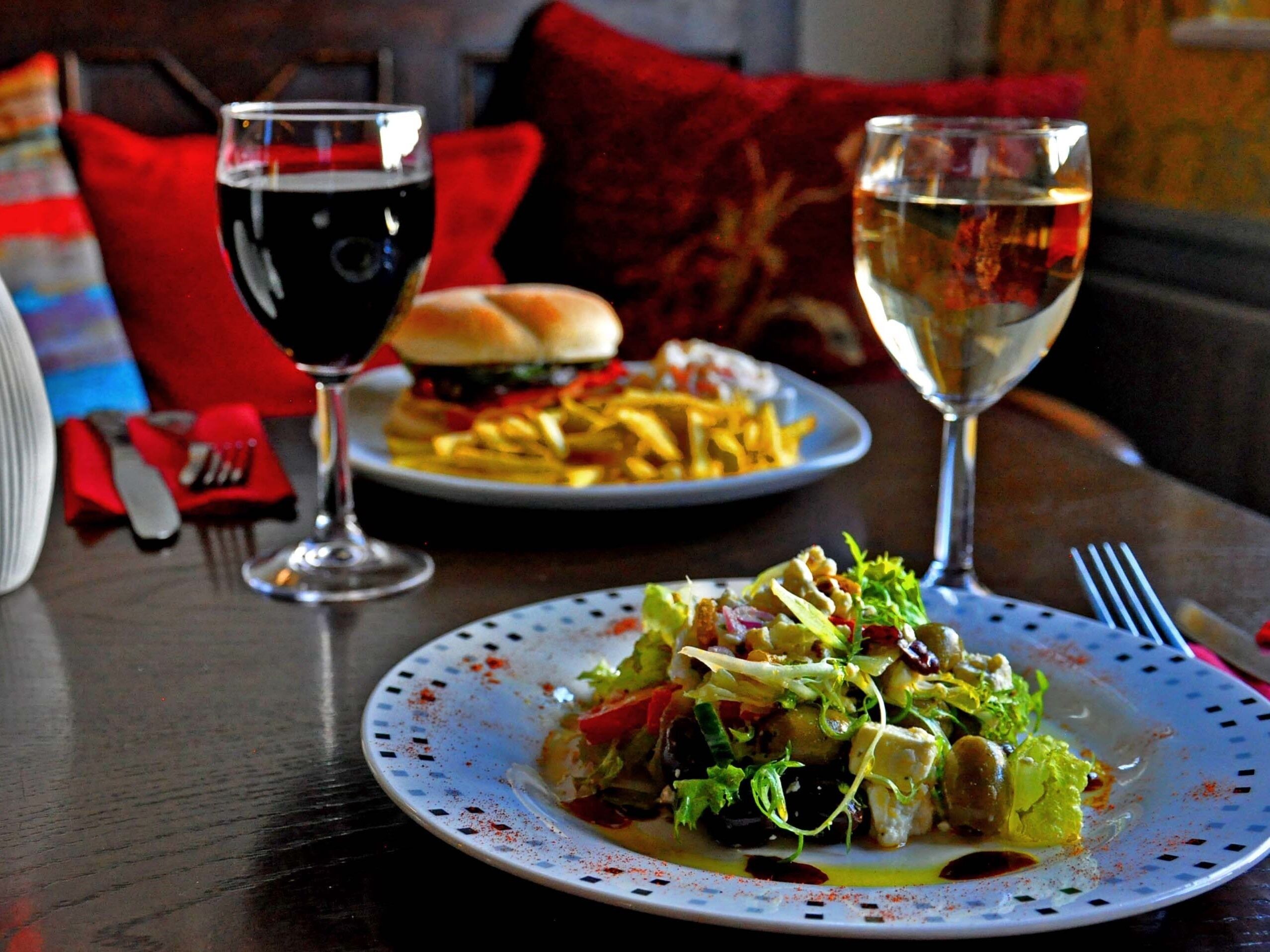 Uma mesa de jantar com um prato de comida, uma taça de vinho tinto e uma taça de vinho branco.