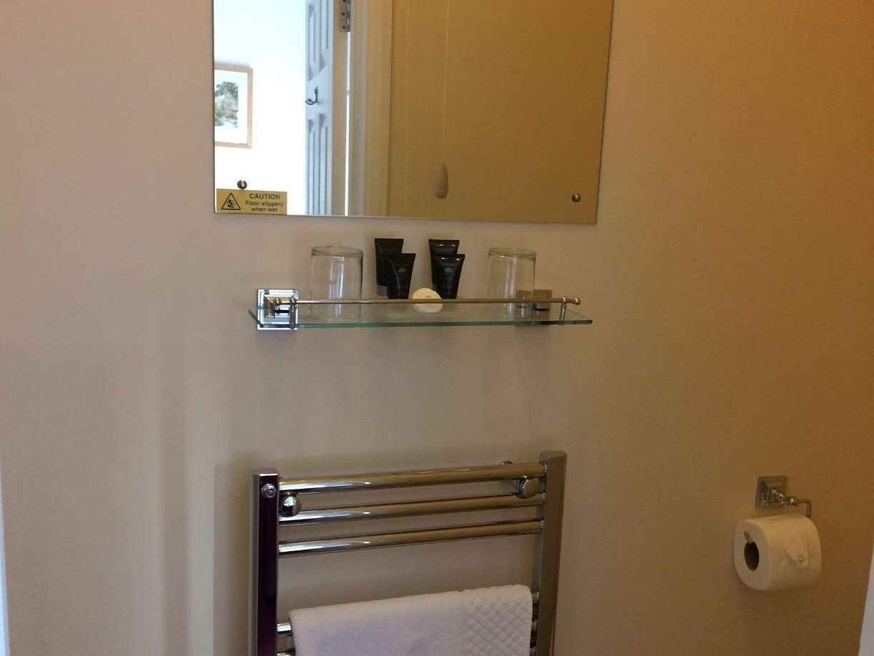 Een badkamer met een glazen plankje met toiletartikelen, een handdoekrek met een witte handdoek en een toiletrolhouder.