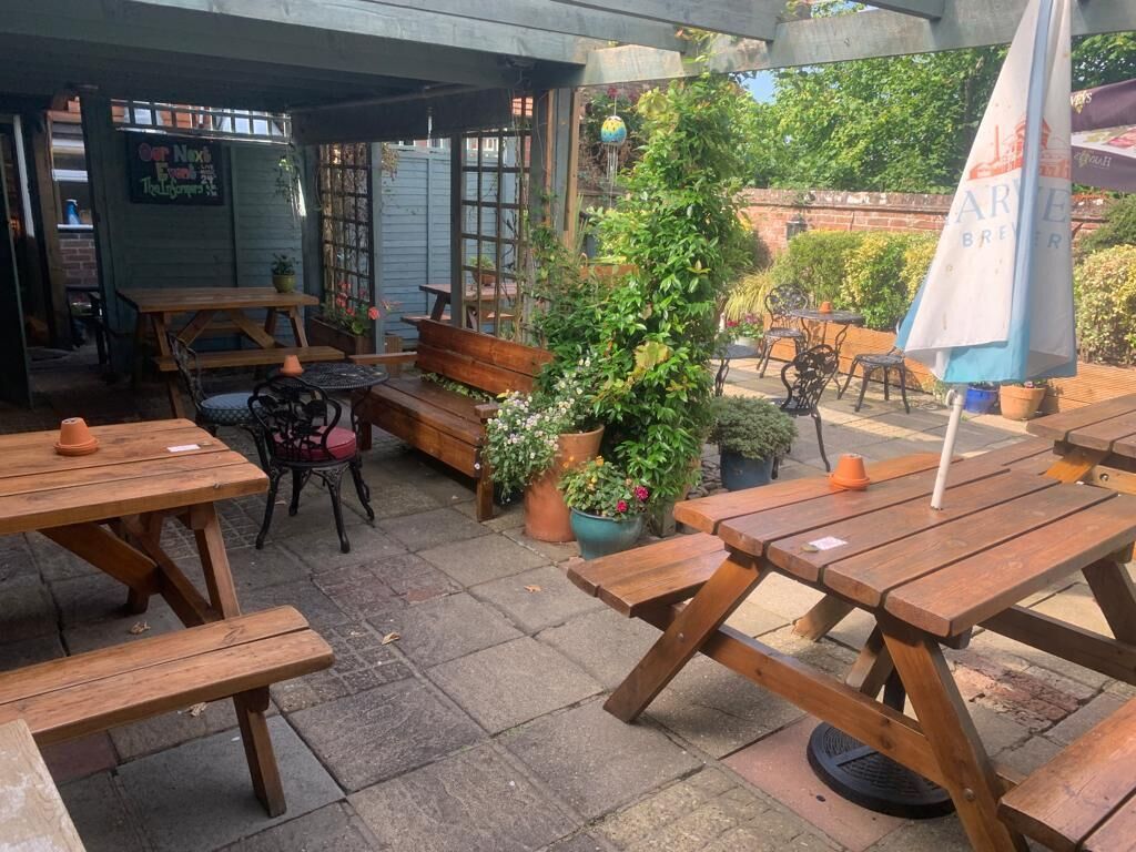 Un espace extérieur aménagé en terrasse, avec des tables et des bancs en bois, entouré de plantes en pot et d’un mur en briques.