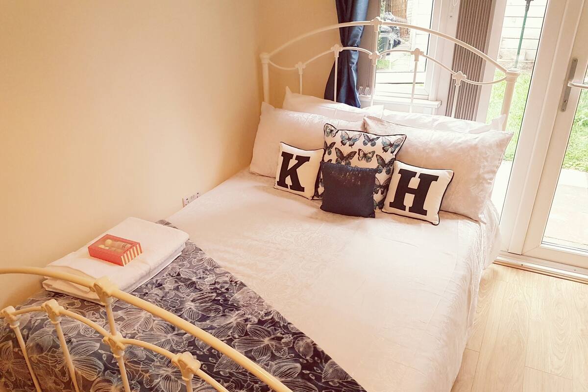 Un lit avec un cadre en métal, une couvre-lit à motifs floraux et des oreillers ornés de grandes lettres.