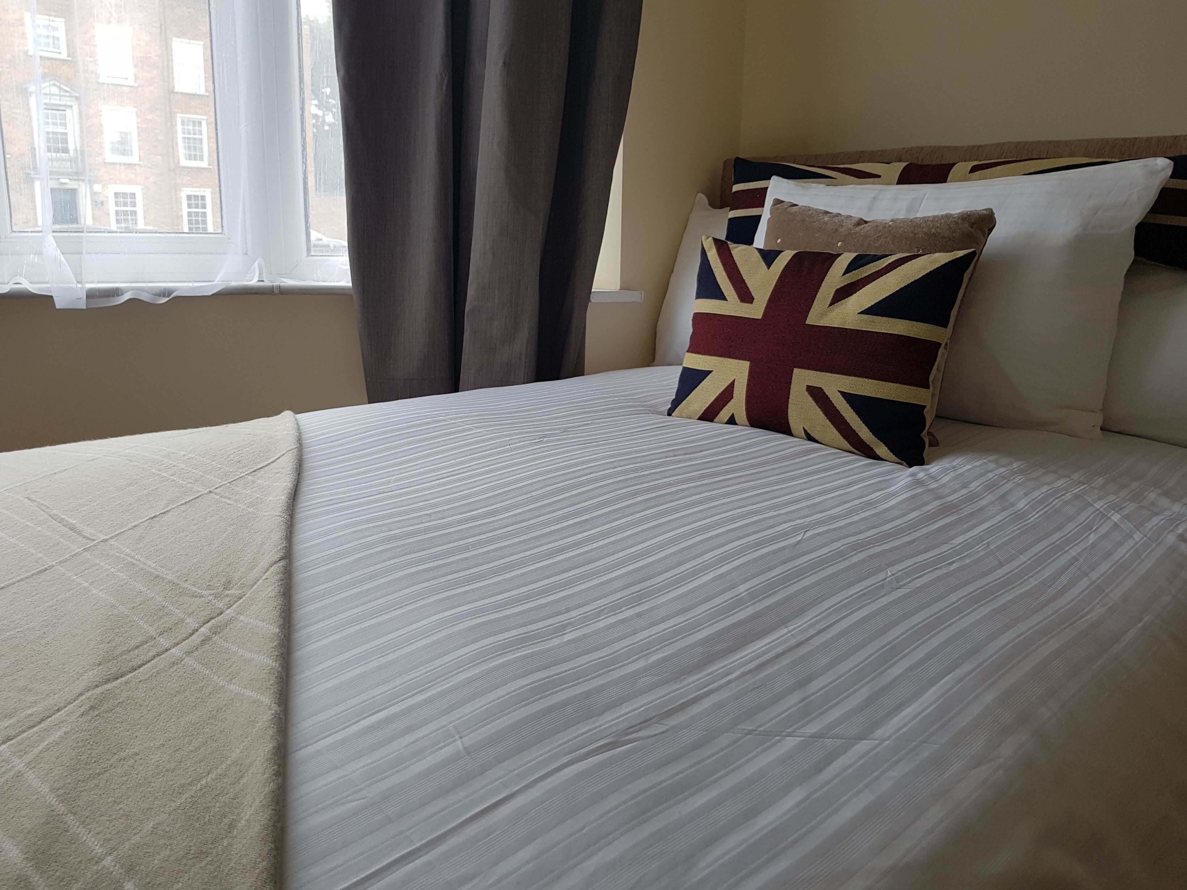 A neatly made bed with a striped bedspread and a Union Jack pillow.