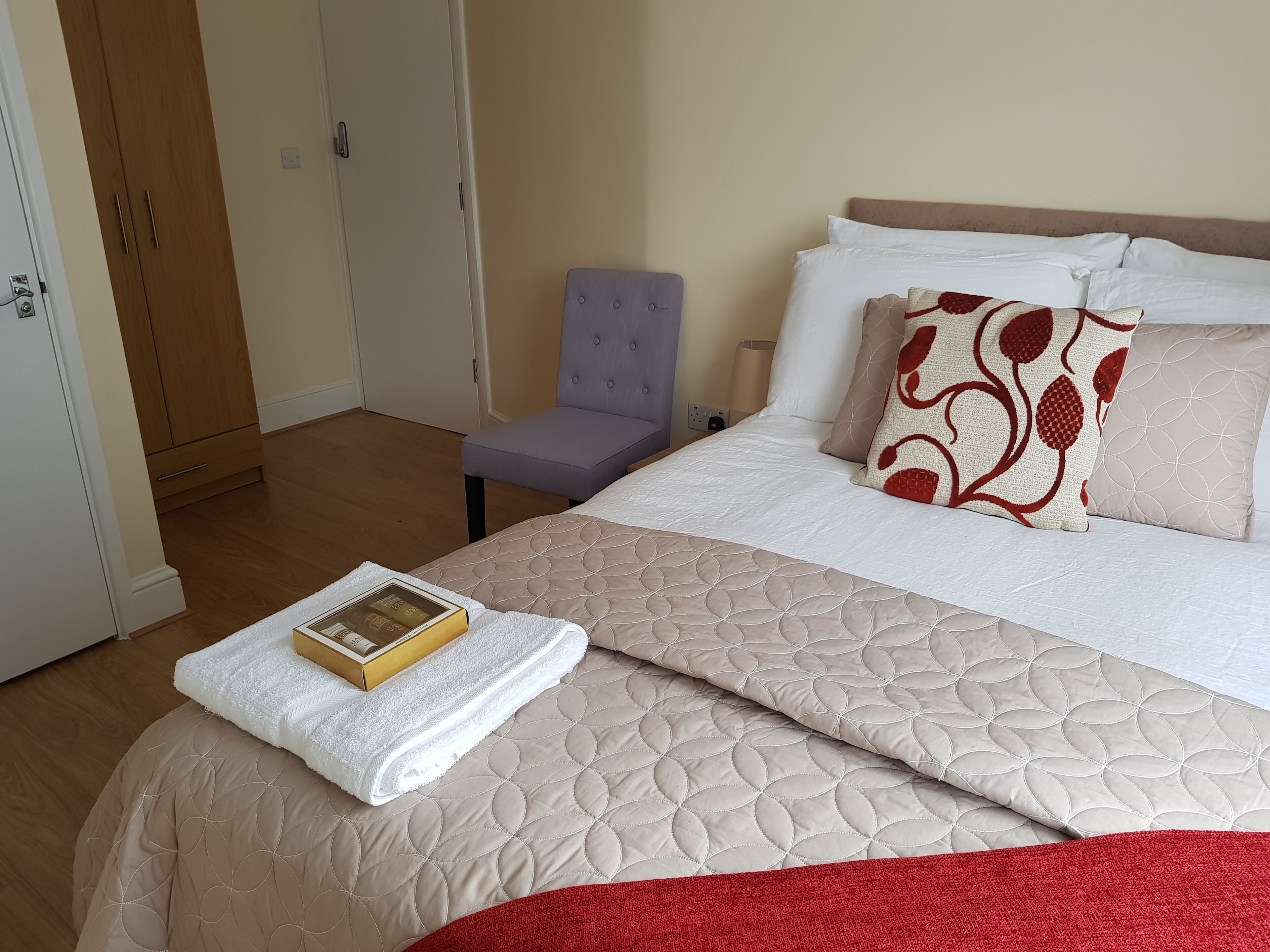 A neatly made bed with a quilted cover, a pillow with a red pattern, and a book on a white towel.