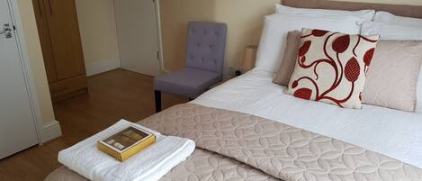 A neatly made bed with a quilted cover, a pillow with a red pattern, and a book on a white towel.