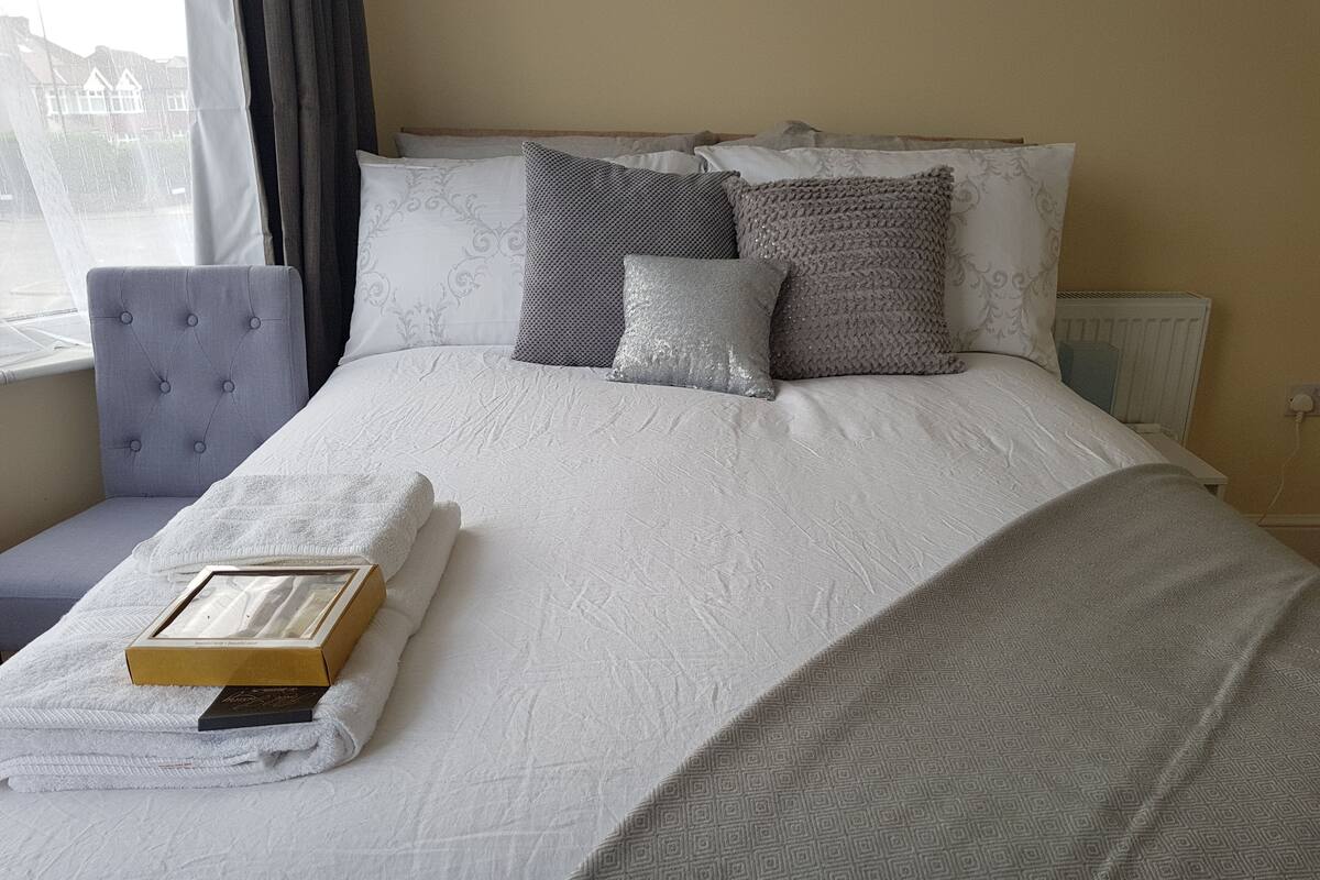Un lit bien fait, avec une couvre-lit à motifs, plusieurs oreillers et une serviette pliée posée sur une table de chevet.