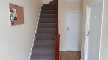 A staircase with carpeted steps and a wooden handrail, leading to a white door with a keypad lock.