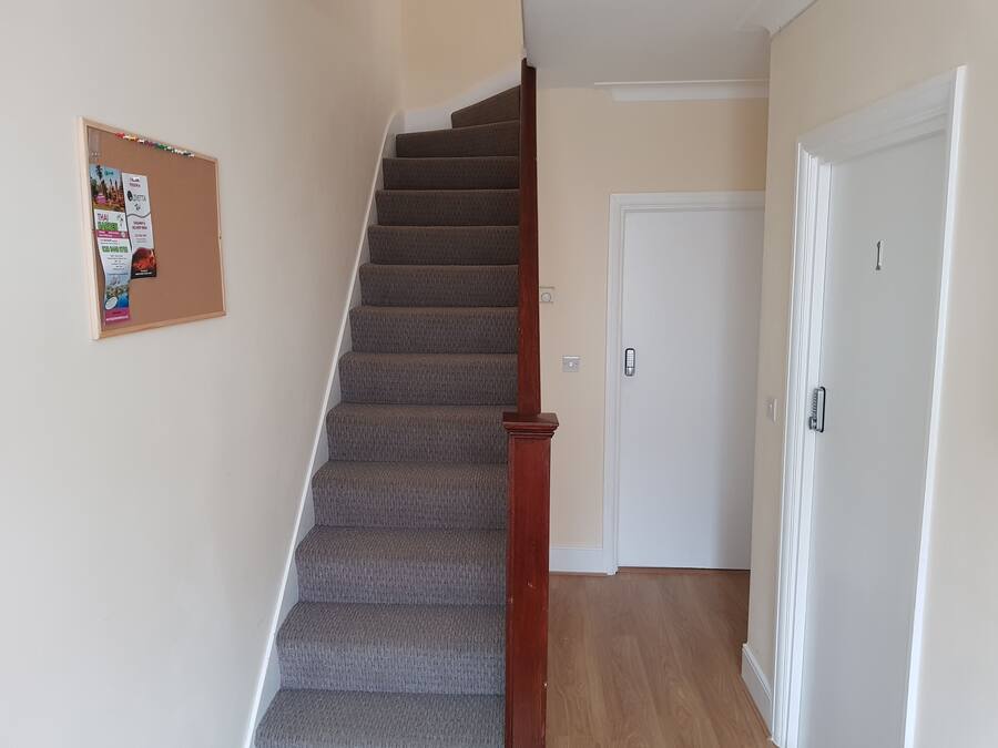 A staircase with carpeted steps and a wooden handrail, leading to a white door with a keypad lock.
