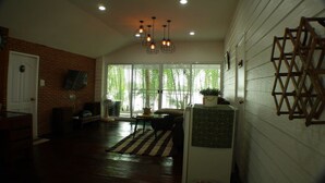 A spacious living room with a brick wall, a large window, and a ceiling light fixture. - River Breeze (Chachoengsao)