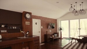 A kitchen with a wooden countertop, a clock, and a brick wall. - River Breeze (Chachoengsao)