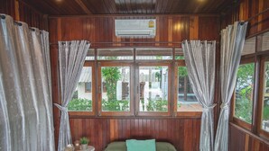 A wooden-paneled room with a bed, a small table, and curtains. - River Breeze (Chachoengsao)