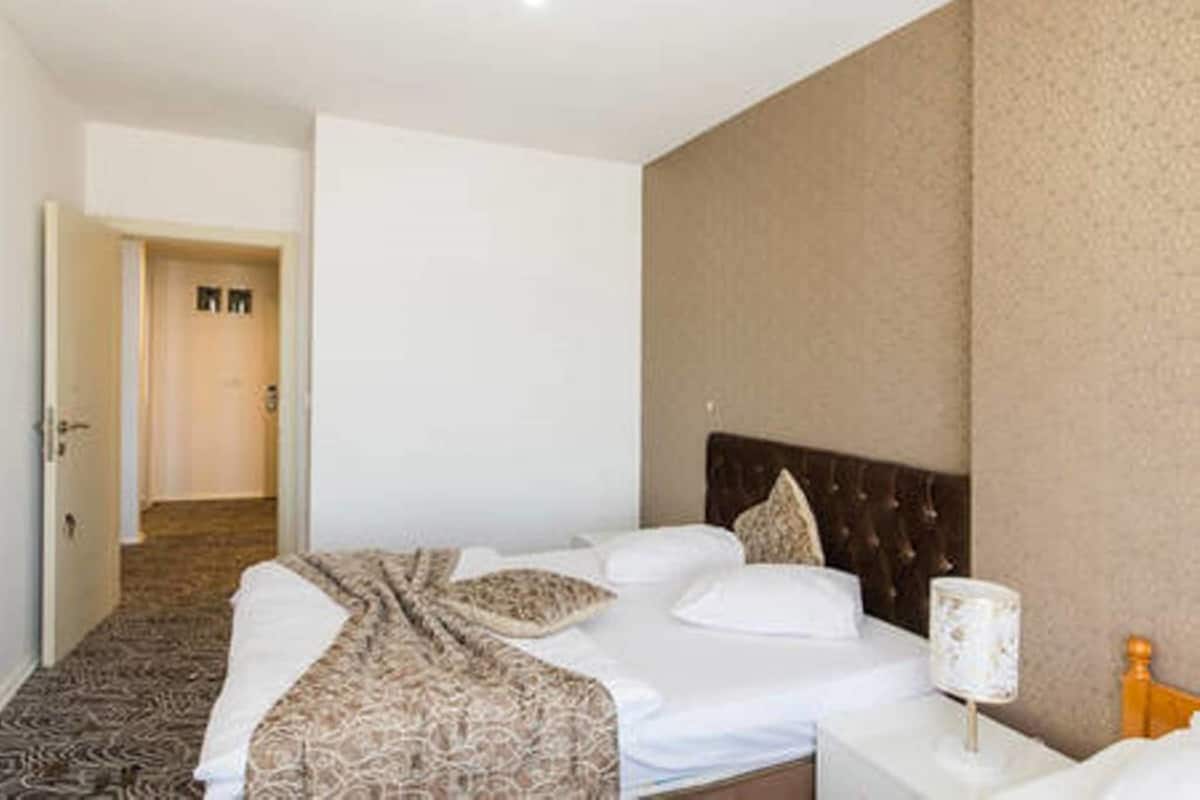 A hotel room with a bed, a nightstand, a lamp, and a door leading to another room.