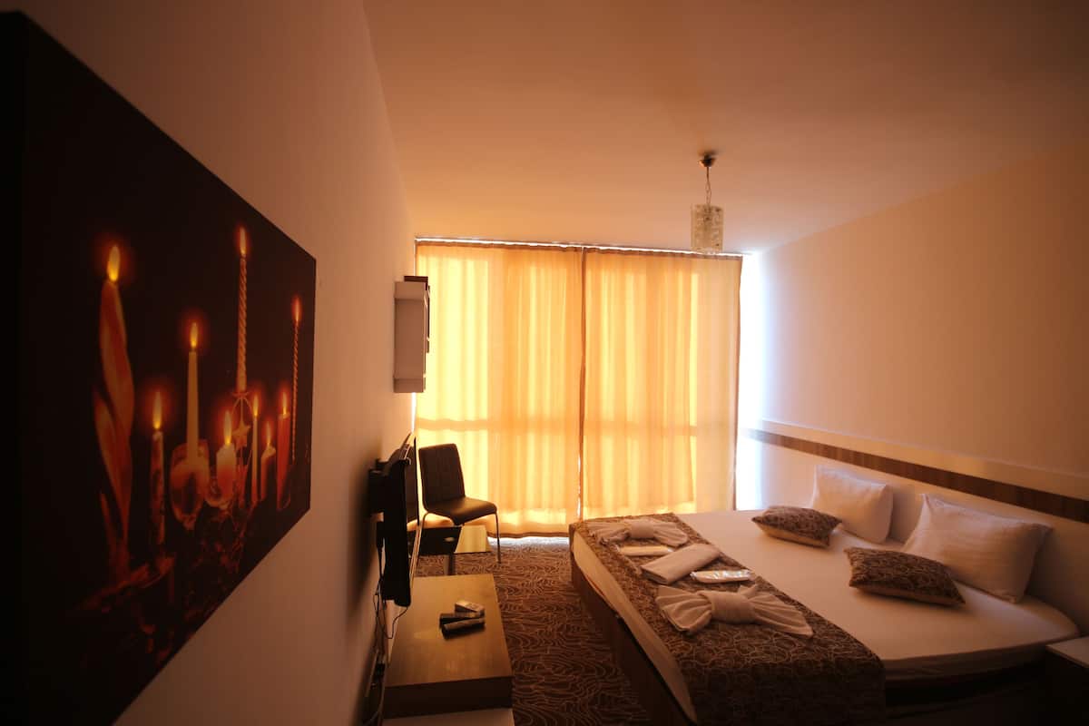 A hotel room with a bed, a desk, a chair, a television, and a painting of candles.