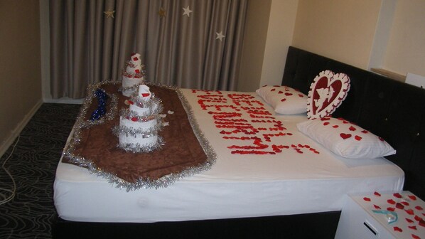 A hotel room with a bed adorned with a heart-shaped bedspread, a small Christmas tree, and a decorative pillow.