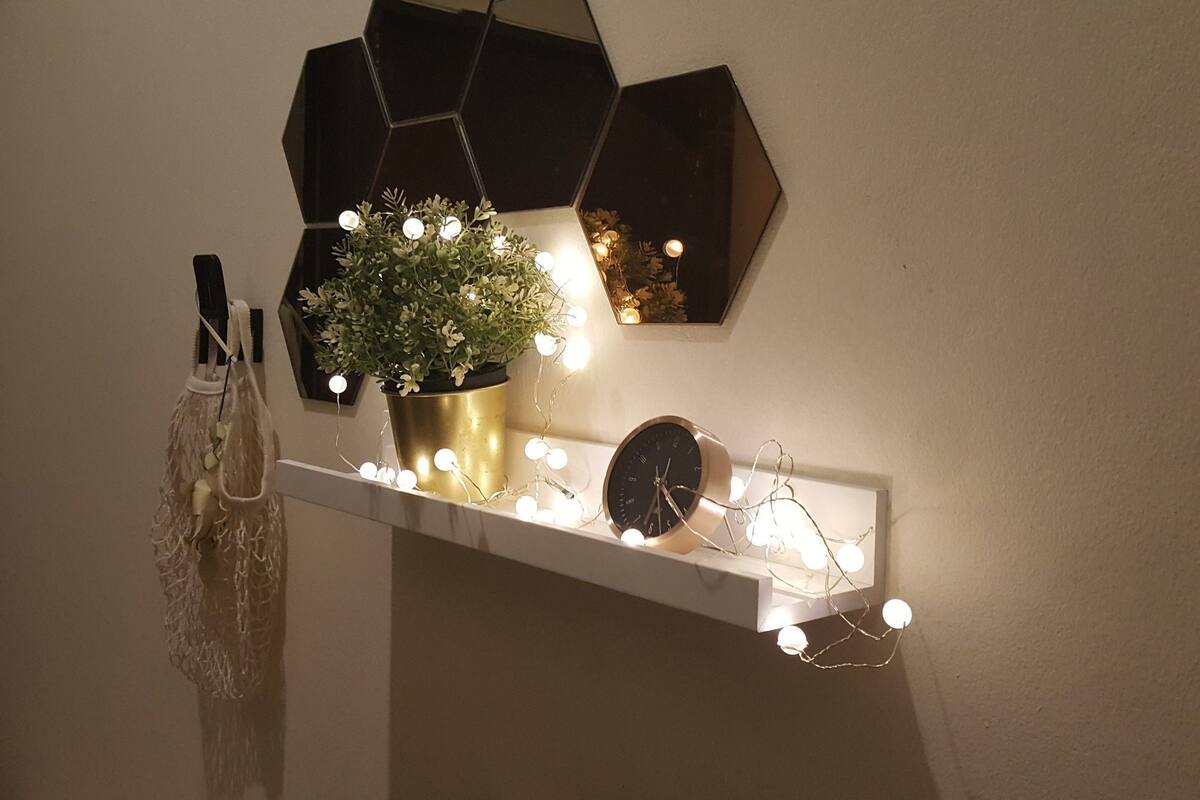 A shelf with a potted plant, a clock, and string lights.