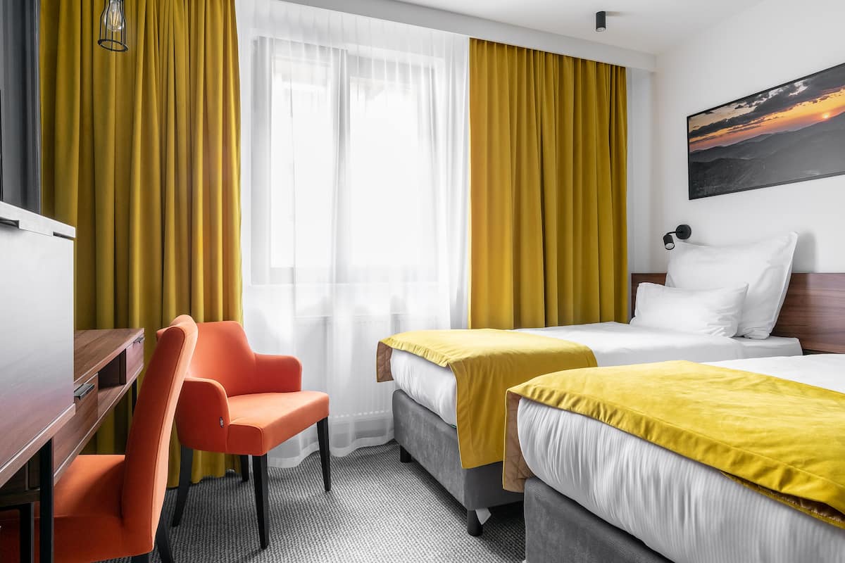 Habitación de hotel con dos camas, un escritorio y una silla naranja.