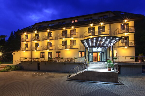A multi-story hotel with a central entrance, outdoor seating area, and balconies.