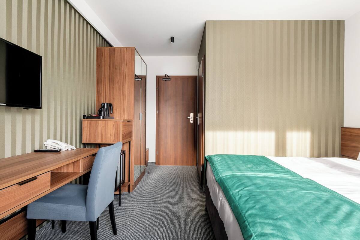 Una habitación de hotel con cama, escritorio, silla, televisor y armario.