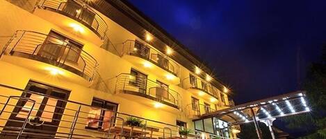 Un hotel de varios pisos con balcones, mobiliario exterior y una escalera que lleva a la entrada.