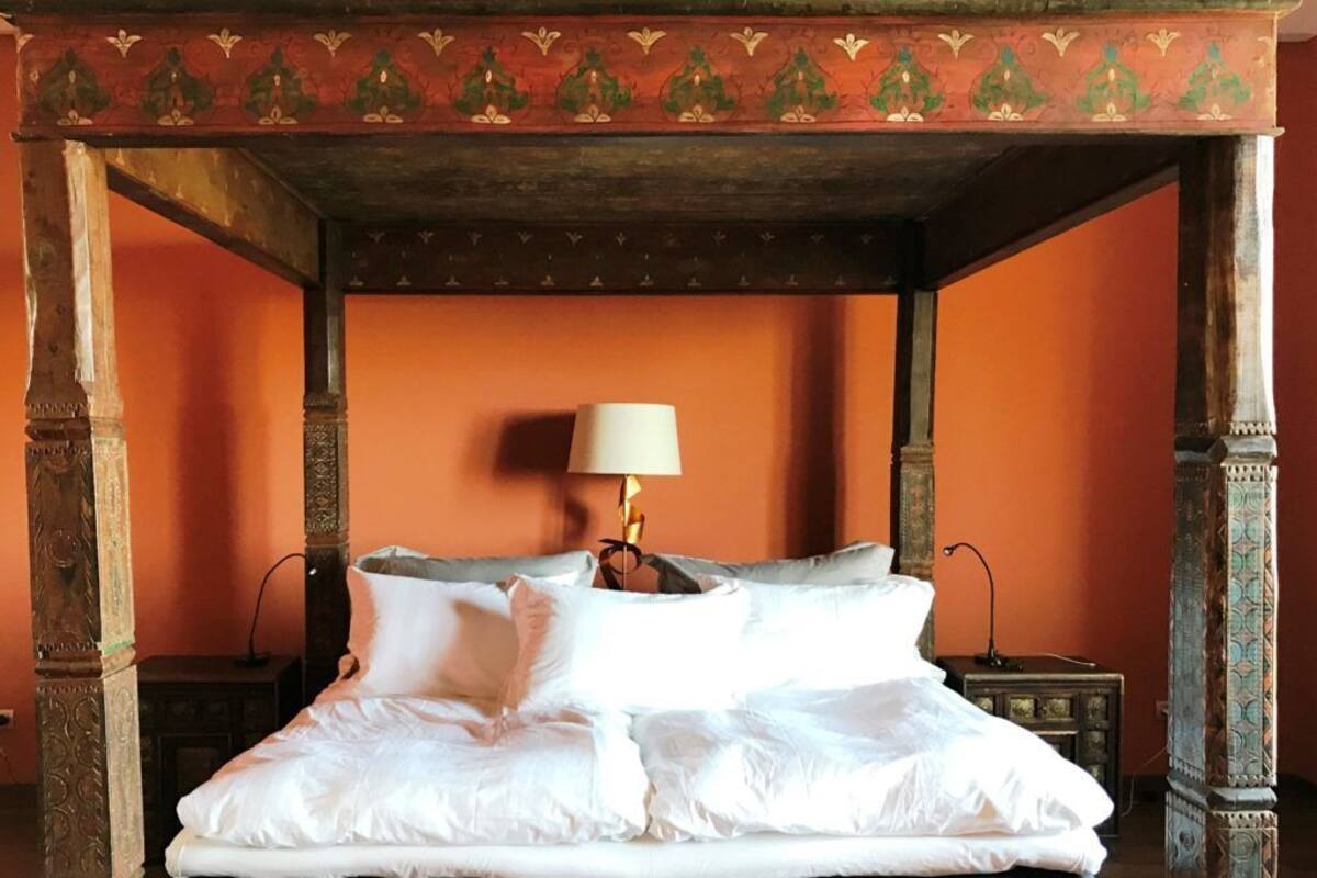 A four-poster bed with white linens and a lamp on a nightstand.