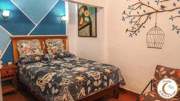 A bedroom with a bed, a nightstand, a chair, and a wall with a tree and bird mural.