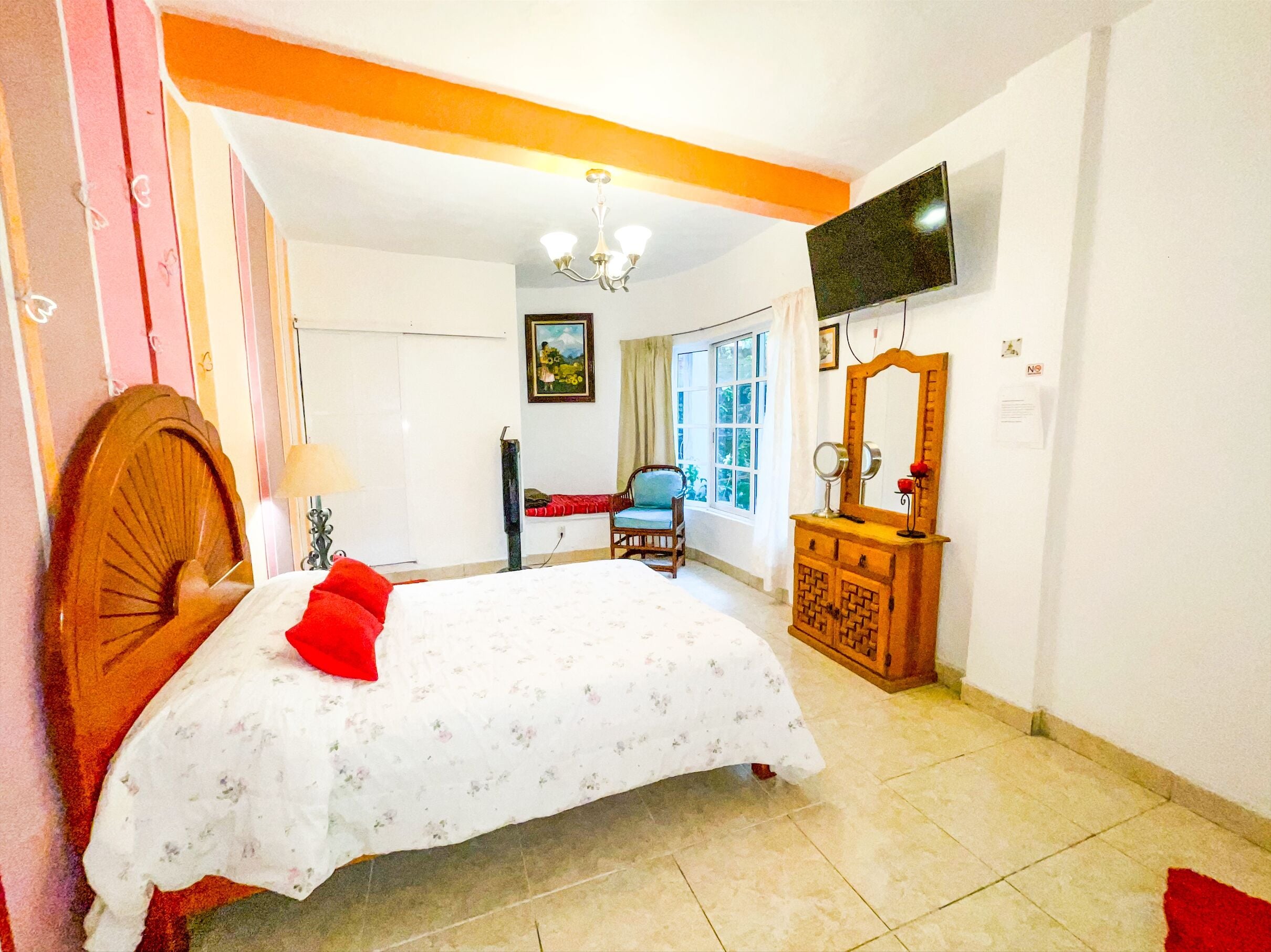 A bedroom with a bed, a dresser, a chair, a TV, and a window.