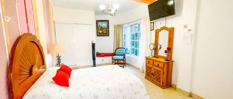 A bedroom with a bed, a dresser, a chair, a TV, and a window.