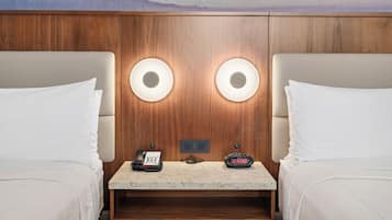 Habitación de hotel con dos camas, una mesita, un teléfono y un reloj digital.