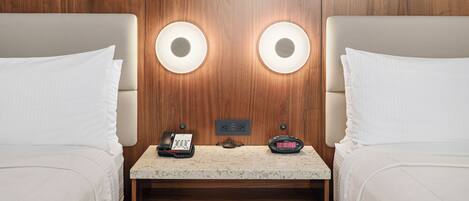 A hotel room with two beds, a small table, a telephone, and a digital clock.