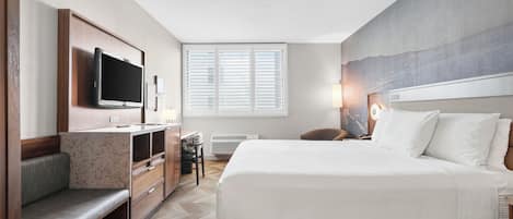A hotel room with a bed, a desk, a TV, a chair, and a window with blinds.