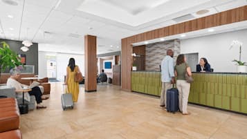 A hotel lobby with a reception desk, seating area, and a large plant.