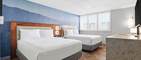 Ein Hotelzimmer mit einem großen Bett, einem kleineren Bett, einem Schreibtisch und Blick auf die Stadt durch das Fenster.