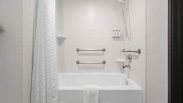 A modern bathroom with a white bathtub, grab bars, a showerhead, and toiletries on a shelf.