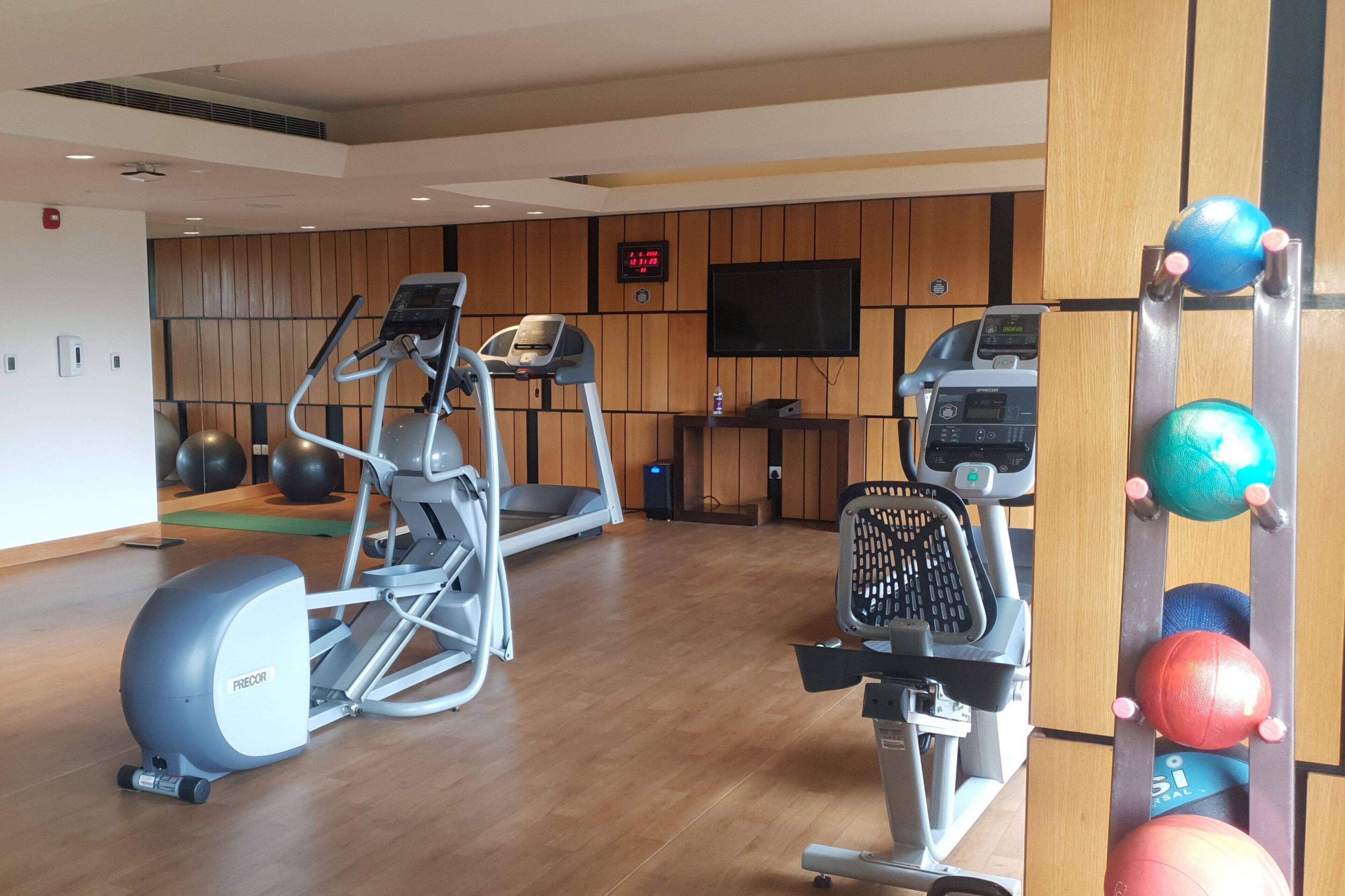 Une salle de sport équipée de machines de cardio, d’un téléviseur et de ballons d’exercice.